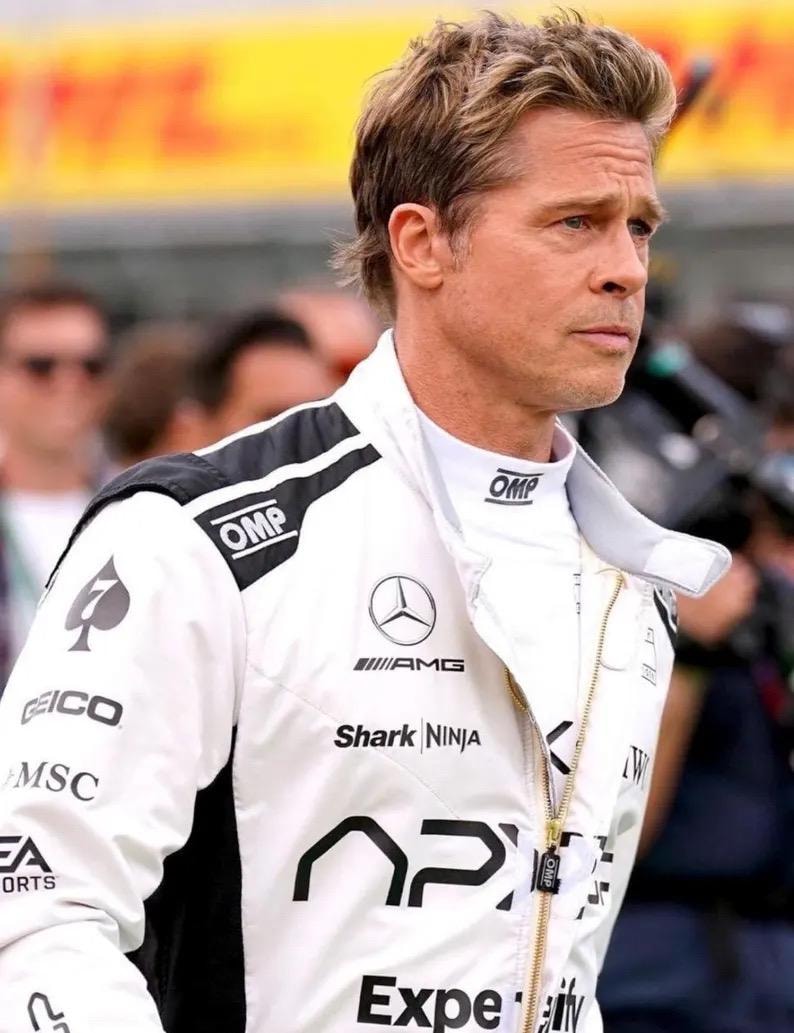 Puede incluir: Chaqueta de carreras blanca con detalles negros, con logotipos de OMP, AMG, Shark Ninja y AP. La chaqueta tiene una cremallera dorada y la lleva una persona con cabello casta&ntilde;o claro.