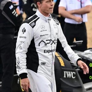 Puede incluir: Un mono de carreras blanco con detalles negros y logotipos de patrocinadores como "GEICO", "MSC" y "APX". El logotipo de Mercedes-AMG y el texto "Shark Ninja" tambi&eacute;n son visibles. La persona est&aacute; cerca de un coche de carreras negro.