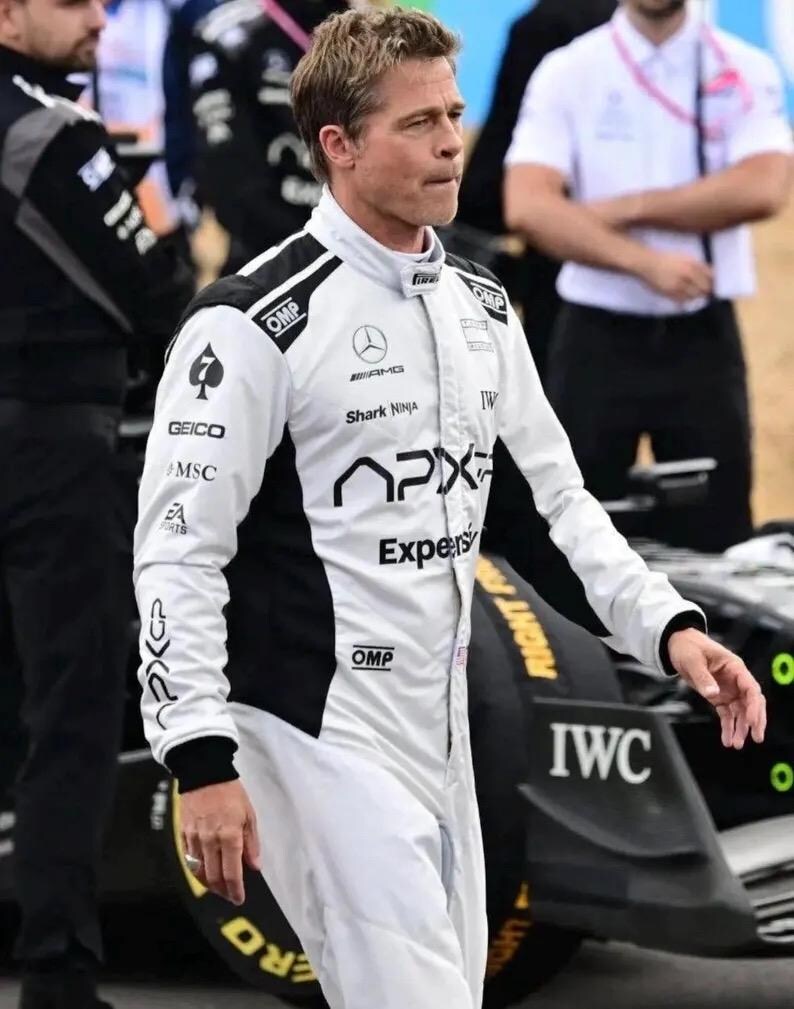 Puede incluir: Un mono de carreras blanco con detalles negros y logotipos de patrocinadores como "GEICO", "MSC" y "APX". El logotipo de Mercedes-AMG y el texto "Shark Ninja" tambi&eacute;n son visibles. La persona est&aacute; cerca de un coche de carreras negro.