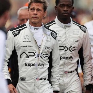 Puede incluir: Dos personas con trajes de carreras blancos con detalles negros y logotipos de patrocinadores. Los trajes tienen los logotipos de AMG, Shark Ninja, IWC y APXGP. Un traje tiene un peque&ntilde;o parche con la bandera estadounidense. Los trajes est&aacute;n cerrados con cremallera y tienen logotipos de OMP.