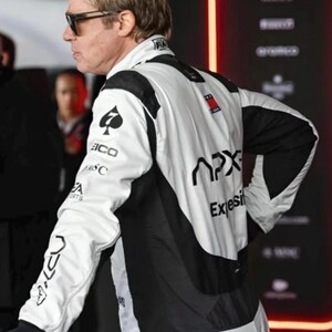 Puede incluir: Chaqueta de carreras blanca y negra con logotipos de patrocinadores en las mangas y la espalda. La chaqueta tiene un logotipo de pica negro en la manga izquierda y la palabra "APX" en la espalda. La chaqueta la lleva una persona con gafas de sol.