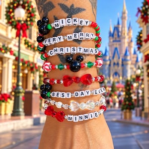 May include: A stack of seven beaded bracelets featuring white letter beads spelling MICKEY, VERY MERRY CHRISTMAS, BEST DAY EVER, and MINNIE. The bracelets include red, green, and silver beads, black Mickey Mouse icons, red and clear bows.