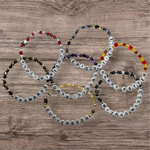 以下が含まれることがあります： さまざまなテーマのビーズブレスレットのコレクション。ブレスレットには、「Hogwarts」、「Butterbeer」、「Harry Potter World」などのフレーズを綴る白い文字ビーズが付いています。ビーズの色は、赤、黒、黄色など様々です。