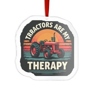 Op de afbeelding: Een doorzichtig, plat ornament met een onregelmatige vorm en een rood lint. Het ontwerp toont een rode tractor tegen een zonsondergang met horizontale strepen en de tekst TRACTORS ARE MY THERAPY in een crèmekleurig lettertype.