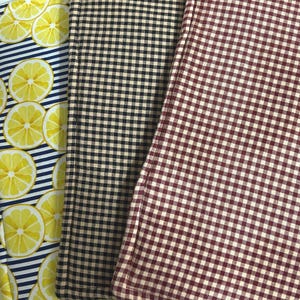 May include: Three fabric items with different patterns. One has yellow lemon slices on a blue and white striped background. Another has a black and tan checkered pattern. The third has a red and white checkered pattern.