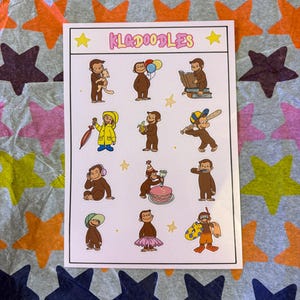 Op de afbeelding: Een stickervel met illustraties van een bruine aap in verschillende poses. De sheet heeft de tekst "KLAODDLES" bovenaan. De aap wordt getoond met een kat, ballonnen, een boek, een banaan en een honkbalknuppel.