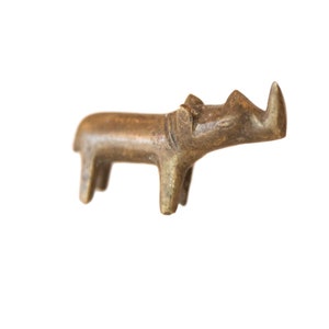 May include: A small, brown, wooden rhinoceros figurine. The figurine is carved in a simple, stylized manner, with a long, pointed horn and a rounded body.