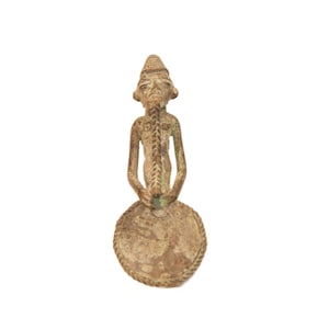 May include: A bronze sculpture of a person holding a round object. The sculpture is detailed and has a weathered finish.