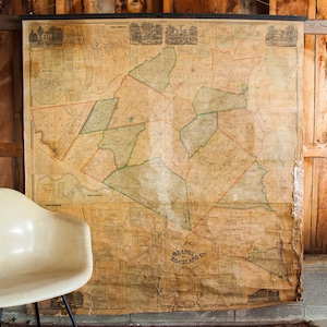 May include: A vintage map of Orange, New Jersey, with a faded, cream-colored background and green lines outlining the different districts. The map is mounted on a wooden frame and hangs on a wall.