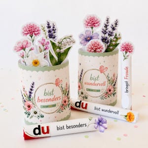 May include: Two cylindrical containers decorated with floral illustrations and the German text "bist besonders" and "bist wundervoll." Two rolled paper tubes feature the text "du bist besonders" and "du bist wundervoll" with floral accents.