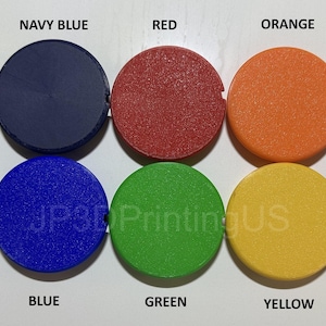 May include: A collection of ten round, colored objects, each with a small notch. Colors include black, navy blue, red, orange, white, blue, green, yellow, and silver. The text "JP3DPrintingUS" is visible.
