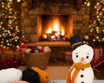 May include: A crocheted snowman with a black top hat and orange scarf sits on a wooden surface. The snowman has black button eyes and a carrot nose. Yarn and crochet supplies are nearby, suggesting a handmade craft project.