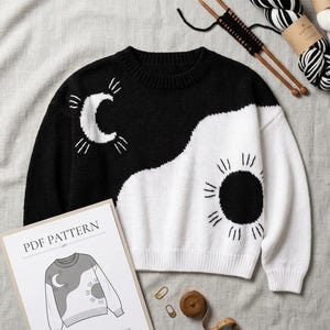 May include: A black and white knit sweater featuring a crescent moon and sun design. The sweater is accompanied by two wooden knitting needles, a skein of black and white yarn, two stitch markers, a measuring tape, and a PDF pattern document.