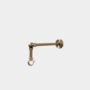 May include: A brass-colored, wall-mounted coat hook. The hook has a curved design and is attached to a horizontal bar. The bar connects to a circular mounting plate with three screw holes. The hook is made of metal and has a vintage aesthetic.