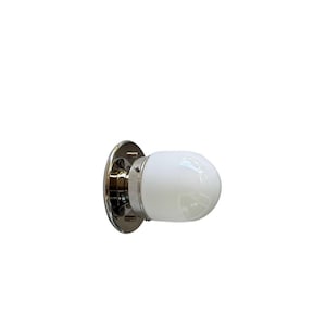 May include: A wall-mounted light fixture featuring a polished chrome circular base and a smooth, rounded white glass globe shade. The metal hardware connects to the glass shade with small, visible screws, creating a clean and functional design.