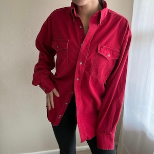 May include: A red button-down shirt with two chest pockets. The long-sleeved shirt has a classic collar and buttoned cuffs. The shirt is made of a soft, durable fabric.