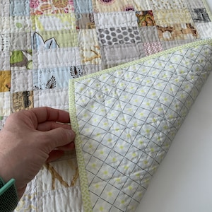 May include: A patchwork quilt with a white background and various colored squares. The quilt is folded in half, revealing a light green and white patterned backing with a lime green border.