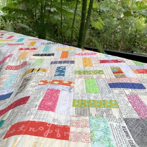 May include: A colourful patchwork quilt featuring a variety of fabrics, including a newspaper print, a floral print, and a polka dot print. The quilt is made in a herringbone pattern.