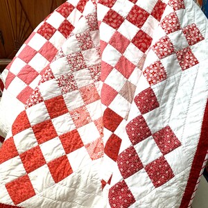 May include: A red and white patchwork quilt with a heart design in the center. The quilt is made of squares of different red and white fabrics.