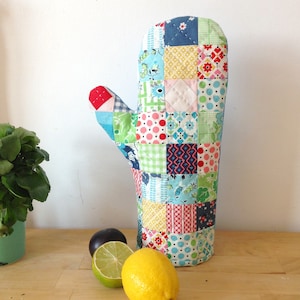 May include: A colorful patchwork oven mitt with a quilted design. The mitt is made of various fabrics in shades of blue, green, red, yellow, and white.