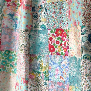 May include: A patchwork fabric with a variety of floral patterns in shades of pink, blue, green, and yellow. The fabric is arranged in a grid pattern, with each square featuring a different design.