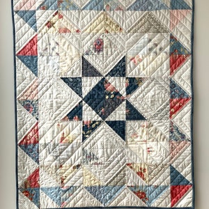 May include: A patchwork quilt with a star design in the centre. The quilt is made of various fabrics in shades of blue, pink, and white. The quilt is quilted with a diamond pattern.
