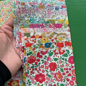 May include: A stack of fabric squares with floral patterns in shades of pink, red, yellow, blue, and green. The fabric squares are arranged in a vertical stack, with the top square being a light green and white floral pattern.
