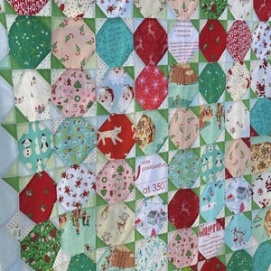 Pode incluir: Um cobertor colorido com tema natalino. O cobertor é feito de vários tecidos com padrões diferentes, incluindo Papai Noel, renas e homens de gengibre. O cobertor também é decorado com as palavras "Gingerbread Man" e "Now Baking at 350 degrees".