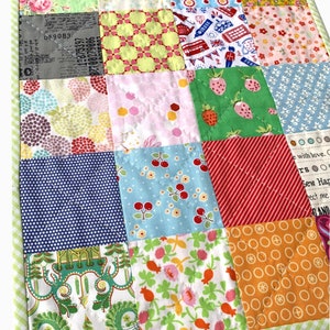 May include: A patchwork quilt featuring a range of colourful fabrics, including floral, geometric and polka dot designs. The quilt is quilted with a crosshatch pattern.