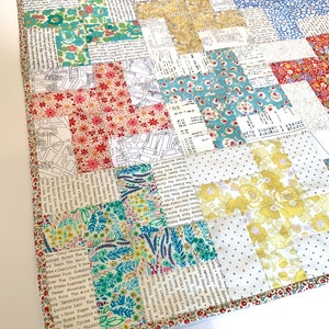 May include: A patchwork quilt with a variety of floral, text, and geometric patterns in shades of red, blue, yellow, and green. The quilt features a floral border and is made of various fabric squares.