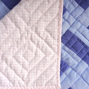 May include: Close-up of a pink and blue quilted fabric. The pink fabric has a gingham pattern and the blue fabric has a checkered pattern.
