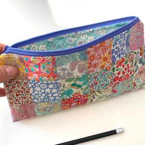 May include: A patchwork fabric pencil case with a blue zipper. The case is made of different floral patterned fabrics.