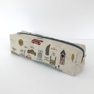 Può includere: Astuccio rettangolare con un design a mappa di Londra. Il tessuto beige presenta illustrazioni di monumenti come il London Eye, il Tower Bridge e un autobus a due piani rosso. Una cerniera blu scuro corre lungo la parte superiore.