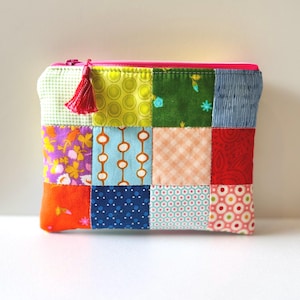 May include: A patchwork zippered pouch with a pink zipper and a red tassel. The pouch is made of various fabric squares in bright colors and patterns, including floral, polka dots, and geometric designs.