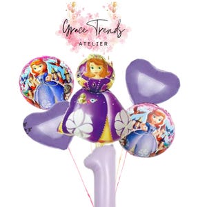 Peut inclure: Un ensemble de ballons violets et à thème de personnages, comprenant des ballons en forme de cœur et ronds représentant une princesse. Un grand ballon numéro un est également inclus, adapté à une célébration du premier anniversaire. Les ballons sont attachés avec une ficelle rouge.