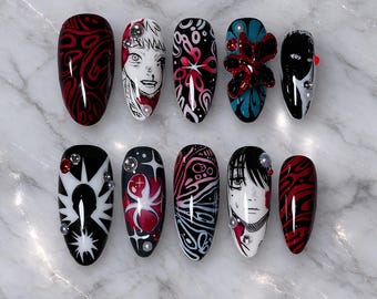 May include: A set of ten artificial nails with various designs. The nails feature a mix of black, white, and red patterns, anime-style character art, and decorative embellishments. Some nails have a glossy finish, while others have matte textures.