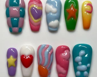 May include: A collection of ten press-on nails with various designs. The nails feature vibrant colors and playful patterns, including a checkerboard, a heart, a star, clouds, and a balloon animal. The nails are glossy and have a rounded shape.