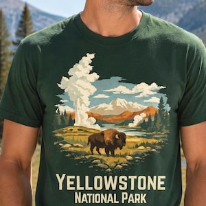 May include: A dark green short-sleeve t-shirt featuring a graphic illustration of a bison standing in a landscape with geysers, mountains, and trees. The text "YELLOWSTONE NATIONAL PARK" is printed in a cream-colored font below the illustration.