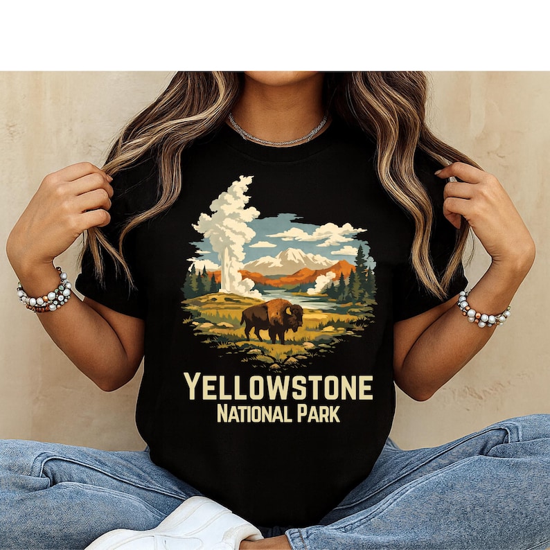 May include: Black t-shirt featuring a Yellowstone National Park design. The graphic depicts a bison in a landscape with mountains, trees, and a geyser. The text "YELLOWSTONE NATIONAL PARK" is printed below the image.