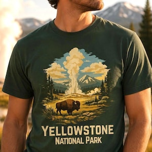 May include: A dark green t-shirt featuring a graphic illustration of a bison standing in a landscape with a geyser erupting in the background, mountains, and pine trees. The text "YELLOWSTONE NATIONAL PARK" is printed in white below the graphic.