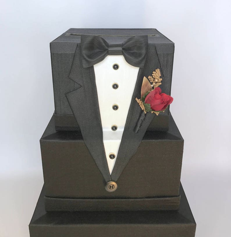 May include: A black card box shaped like a tuxedo with a black bow tie, white shirt front, and a red rose buttonhole.