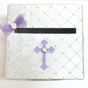 May include: White satin box with a purple cross and a bow with white flowers. The box has a slot for cards or envelopes.