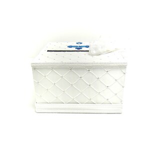 May include: White satin wedding card box with a blue cross design and a diamond pattern. The box has a slot on the top for cards.