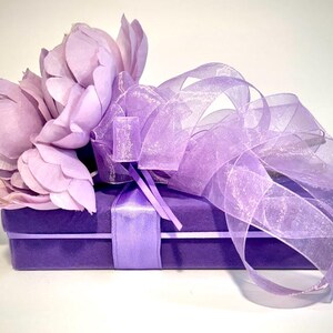 May include: A purple gift box with a satin ribbon and a bouquet of lavender silk flowers tied with a sheer lavender ribbon.