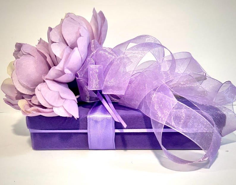May include: A purple gift box with a satin ribbon and a bouquet of lavender silk flowers tied with a sheer lavender ribbon.
