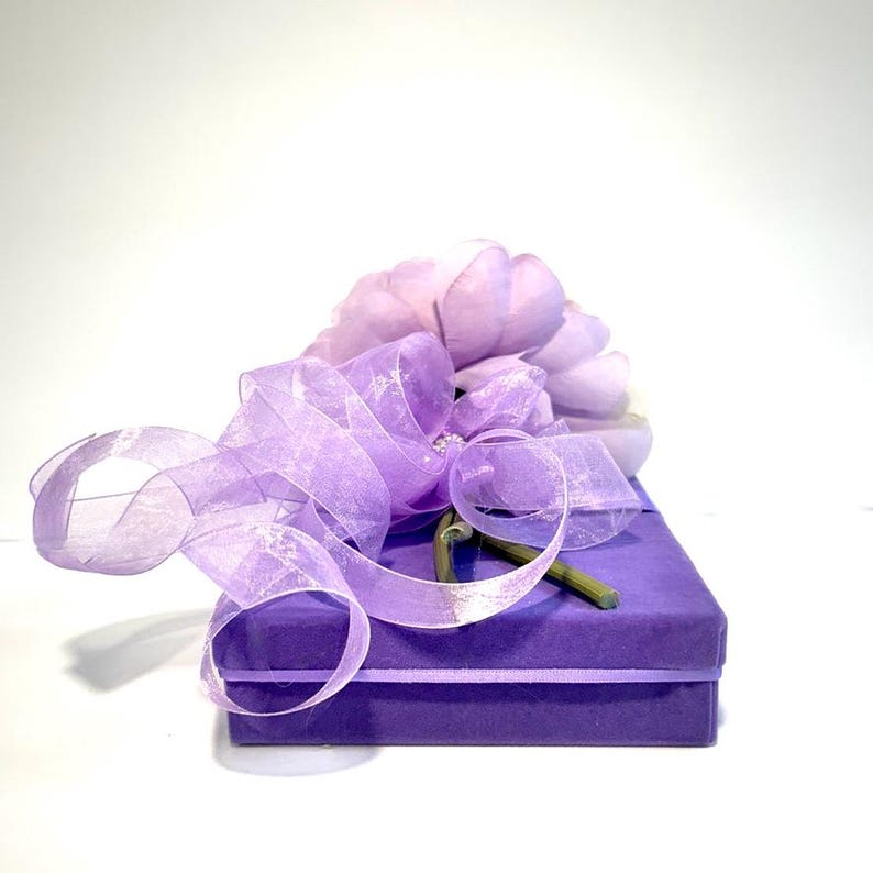 May include: A purple gift box with a lavender ribbon and a single flower on top.