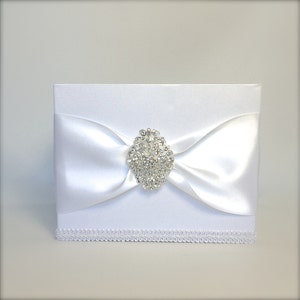 May include: White satin box with a white satin bow and a large silver rhinestone brooch.