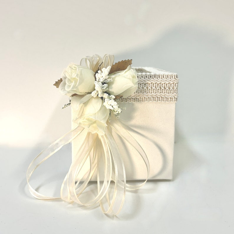 May include: A white gift box with a white satin ribbon and a bouquet of white roses and baby's breath. The box has a white lace trim.