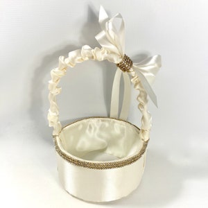 May include: A white satin flower girl basket with a white satin bow and a rhinestone embellishment. The basket has a round base and a handle.