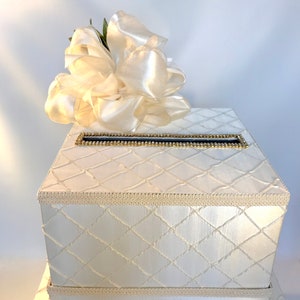 May include: White wedding card box with a large white satin bow on top. The box has a diamond pattern and a gold trim around the top.